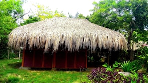 A thatched-roof structure with a red wall, surrounded by greenery. - Las Palmeras (Cartagena)
