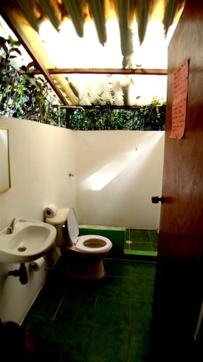 A small bathroom with a toilet, sink, and green tiled floor. - Las Palmeras (Cartagena)