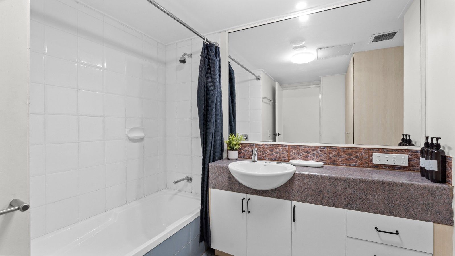 A bathroom with a white bathtub, a sink with a marble countertop, and a mirror above the sink.