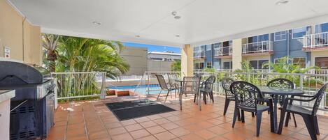 An outdoor patio with a grill, tables, chairs, and a pool.