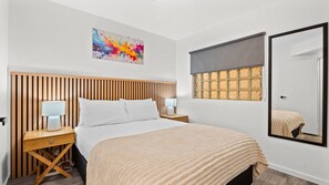 Une chambre à coucher comprenant un lit, des tables de chevet, une commode, une fenêtre avec vue, un tableau accroché au mur et un miroir.