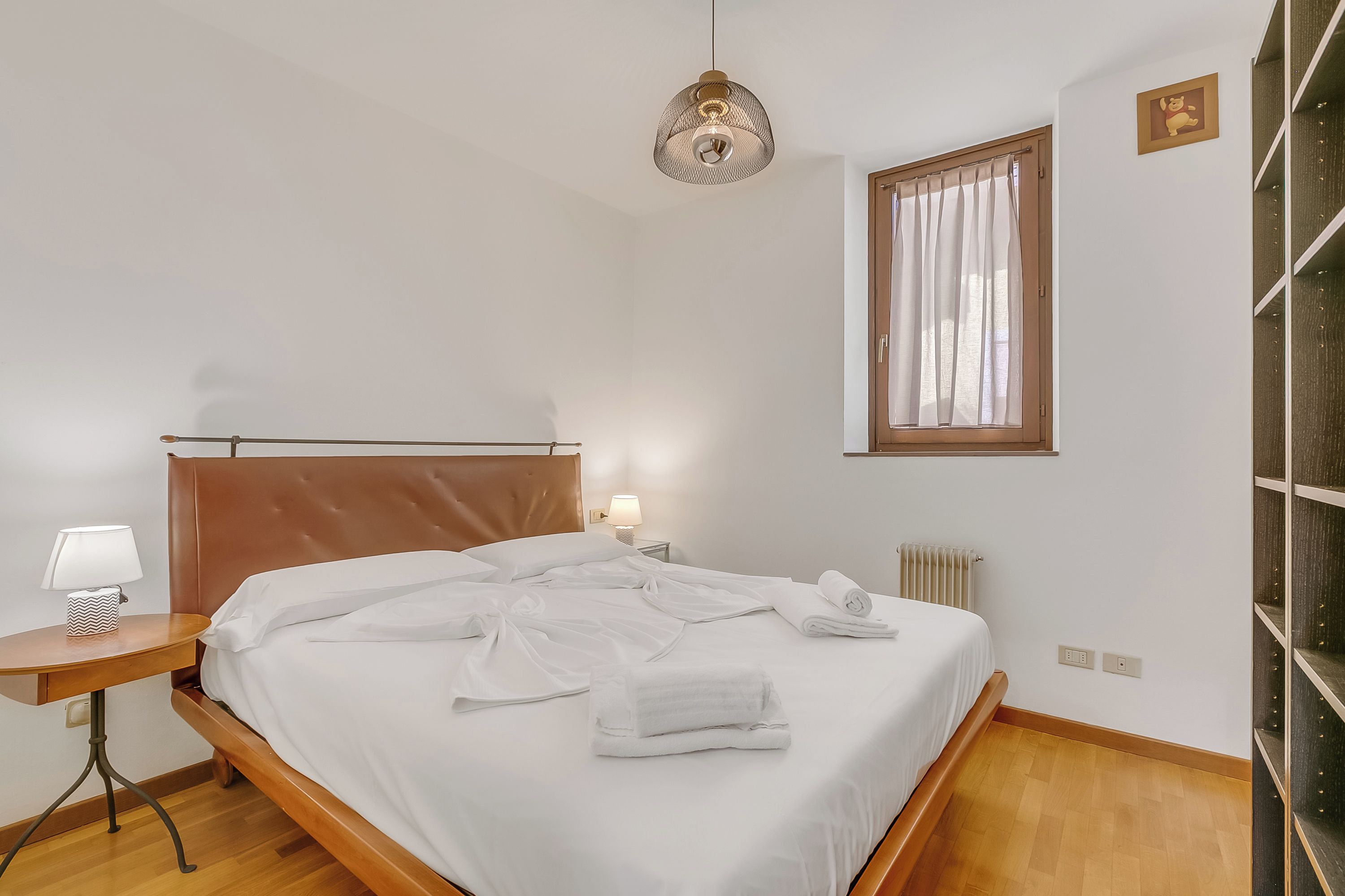 Ein ordentlich bezogenes Bett mit weißen Leinen, eine Nachttischlampe und eine Pendelleuchte.