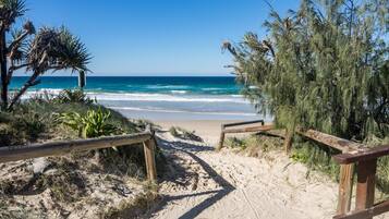 A sandy beach path leading to the ocean with wooden railings and vegetation.