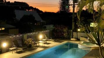 A swimming pool with a hot tub, surrounded by lounge chairs and a railing, with a sunset in the background.