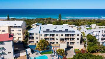 A multi-story hotel with a rooftop pool and solar panels, overlooking a beach and ocean.