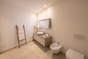 Ein modernes Badezimmer mit einem hölzernen Handtuchhalter, einem großen Spiegel, einem Aufputzbecken, einem Bidet und einer Toilette.