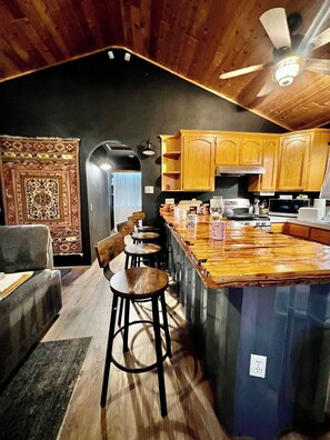 A kitchen with wooden cabinets, a bar area, and a seating space with stools. - ¡De bienvenida! Chalet “Ojo en el cielo”. (Big Bear)