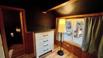 A room with a wooden floor, a white dresser with drawers, a lamp, and a window with curtains.