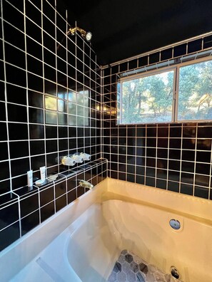 A bathroom with black tiled walls, a bathtub, and a window with a view of trees. - ¡De bienvenida! Chalet “Ojo en el cielo”. (Big Bear)