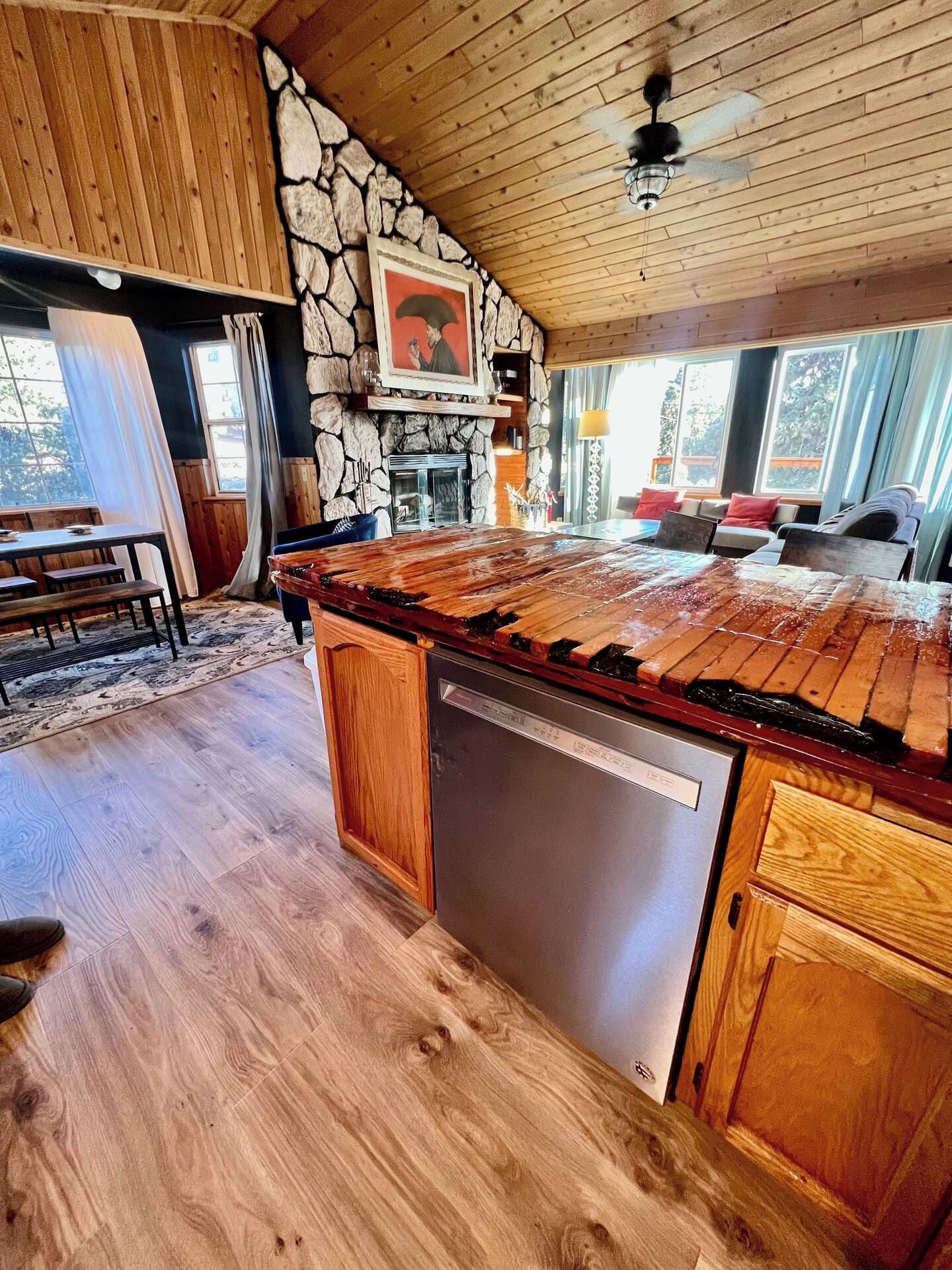 A kitchen with a stone wall, wooden ceiling, and a large island with a dishwasher.