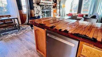 A kitchen with a stone wall, wooden ceiling, and a large island with a dishwasher.