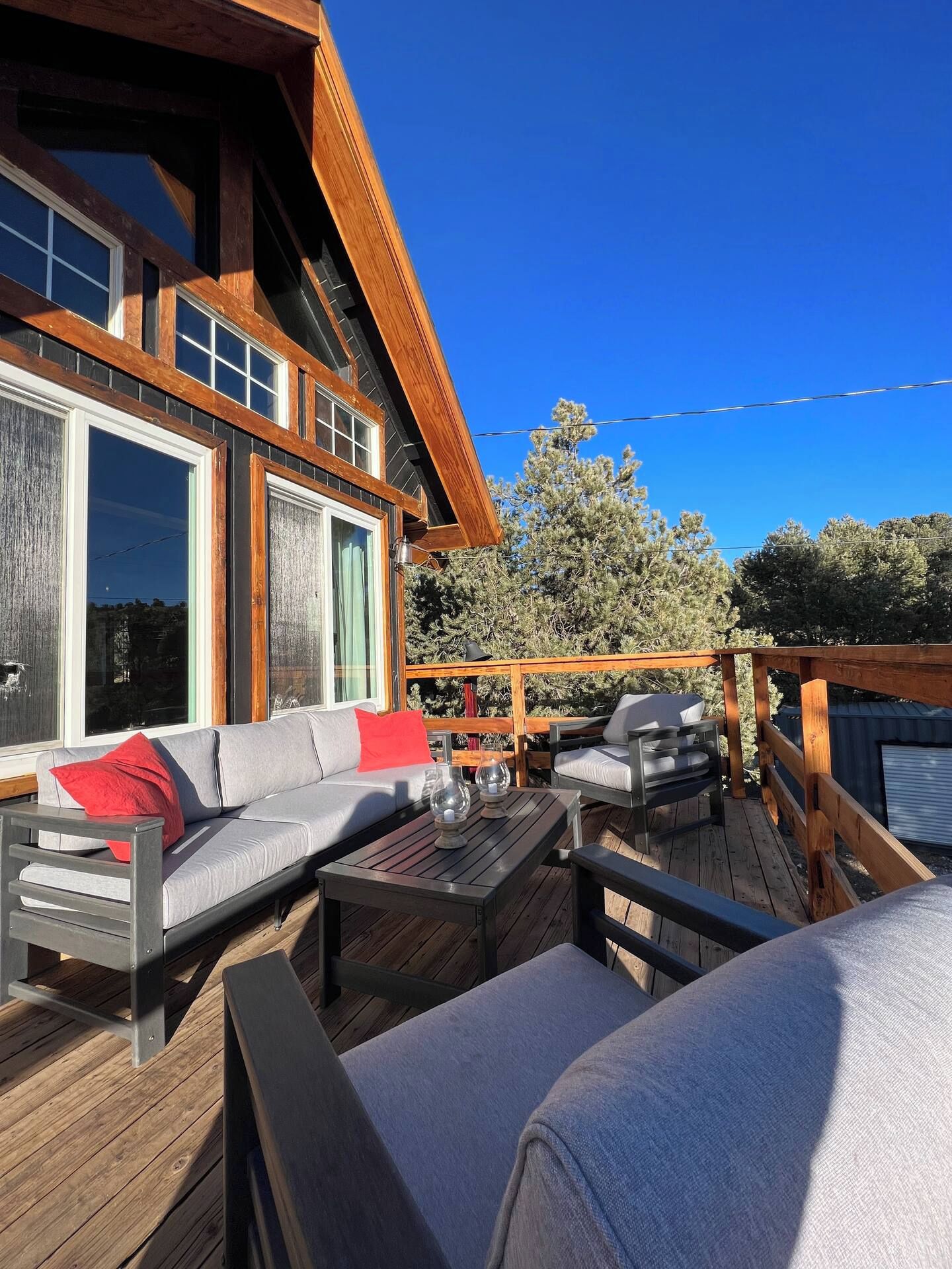 Eine Terrasse mit einer Sitzecke, Sofas, Stühlen und einem Tisch, mit Blick auf ein bewaldetes Gebiet.