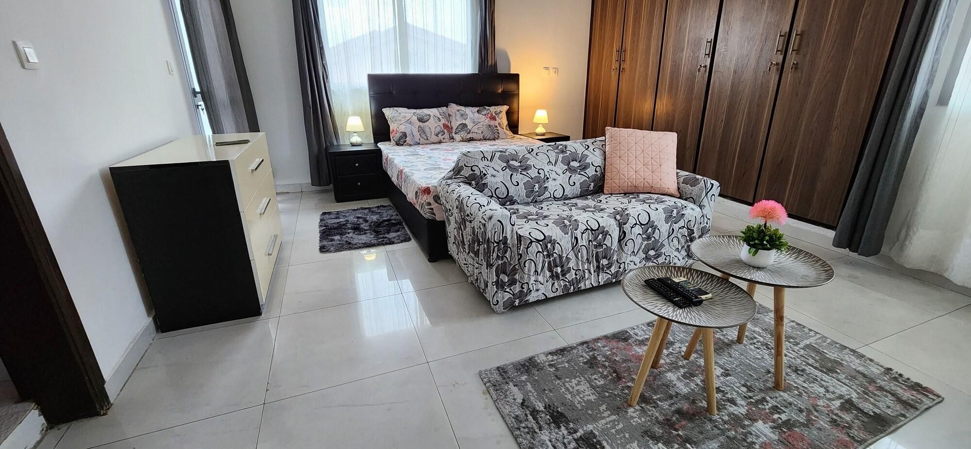 Un dormitorio moderno con cama, mesitas de noche, un pequeño sofá, una mesa de centro y un armario.