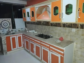 A kitchen with orange cabinets, a gas stove, and a tiled backsplash. - Bhurban Apartments (Bhurban)