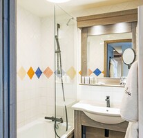 Une salle de bain avec une douche à parois de verre, un lavabo blanc et un miroir avec un cadre en bois.