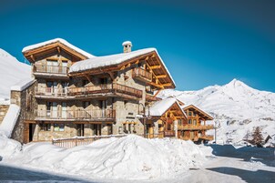 Una cabaña de madera de varios pisos con balcones, frente a un paisaje montañoso nevado.