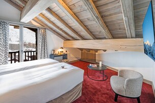 Una habitación con cama, una silla, una mesita y vistas a un paisaje montañoso nevado.
