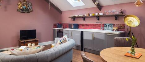 Un espacio habitable compacto con kitchenette, un sofá, una mesa de comedor y una televisión.