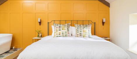Un dormitorio con estructura de cama metálica, cubrecama blanco y dos lámparas fijadas a la pared.
