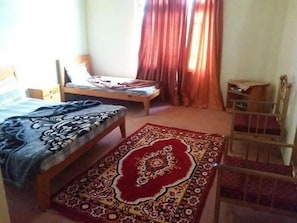 A bedroom with a bed, a smaller bed, a chair, a wooden wardrobe, and a patterned rug.