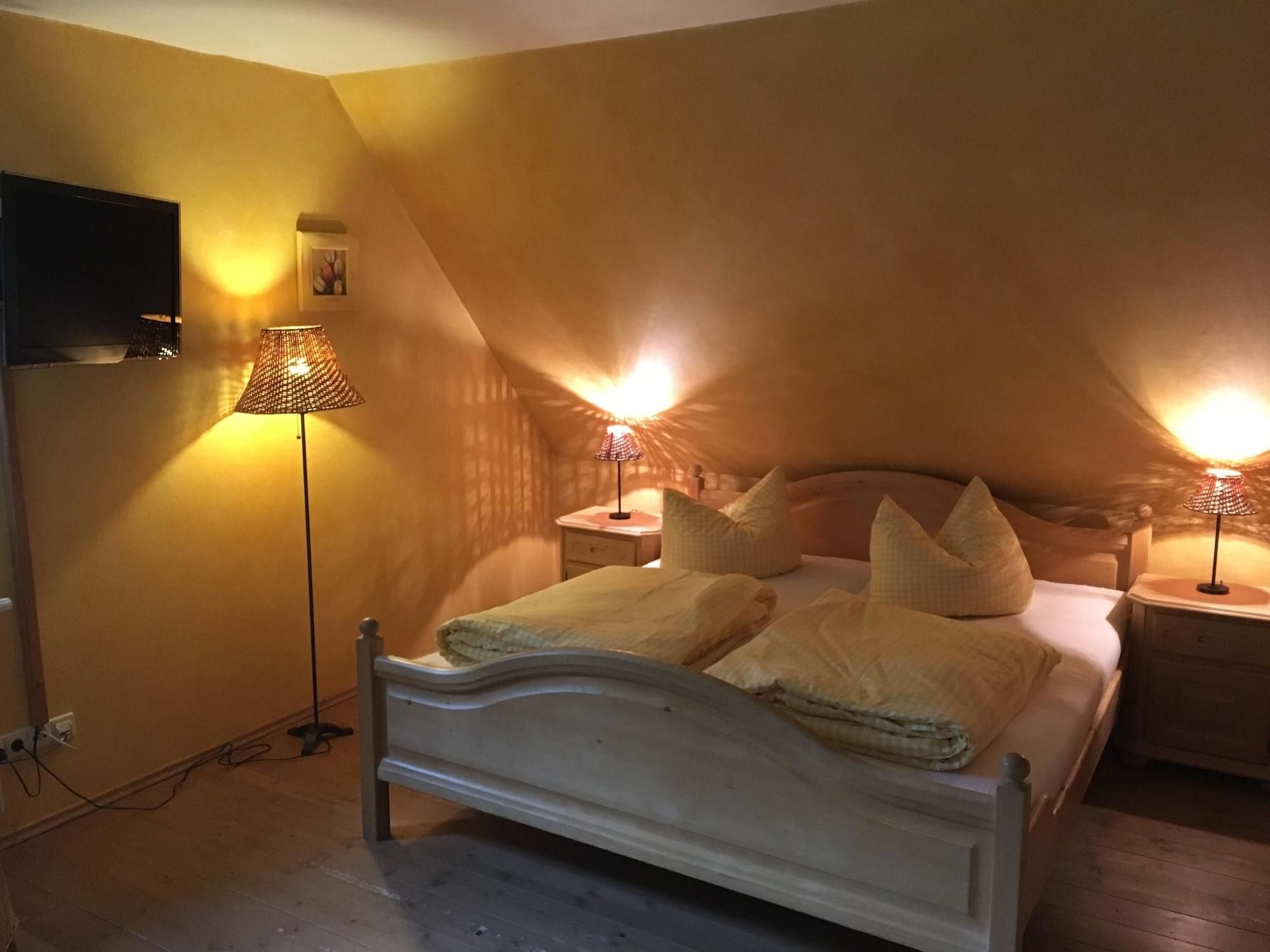 A bedroom with a sloped ceiling, a bed with pillows, two bedside lamps, and a wall-mounted TV.