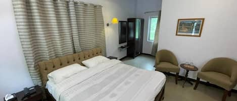 A hotel room with a bed, two armchairs, a small table, a TV, and a framed picture on the wall.