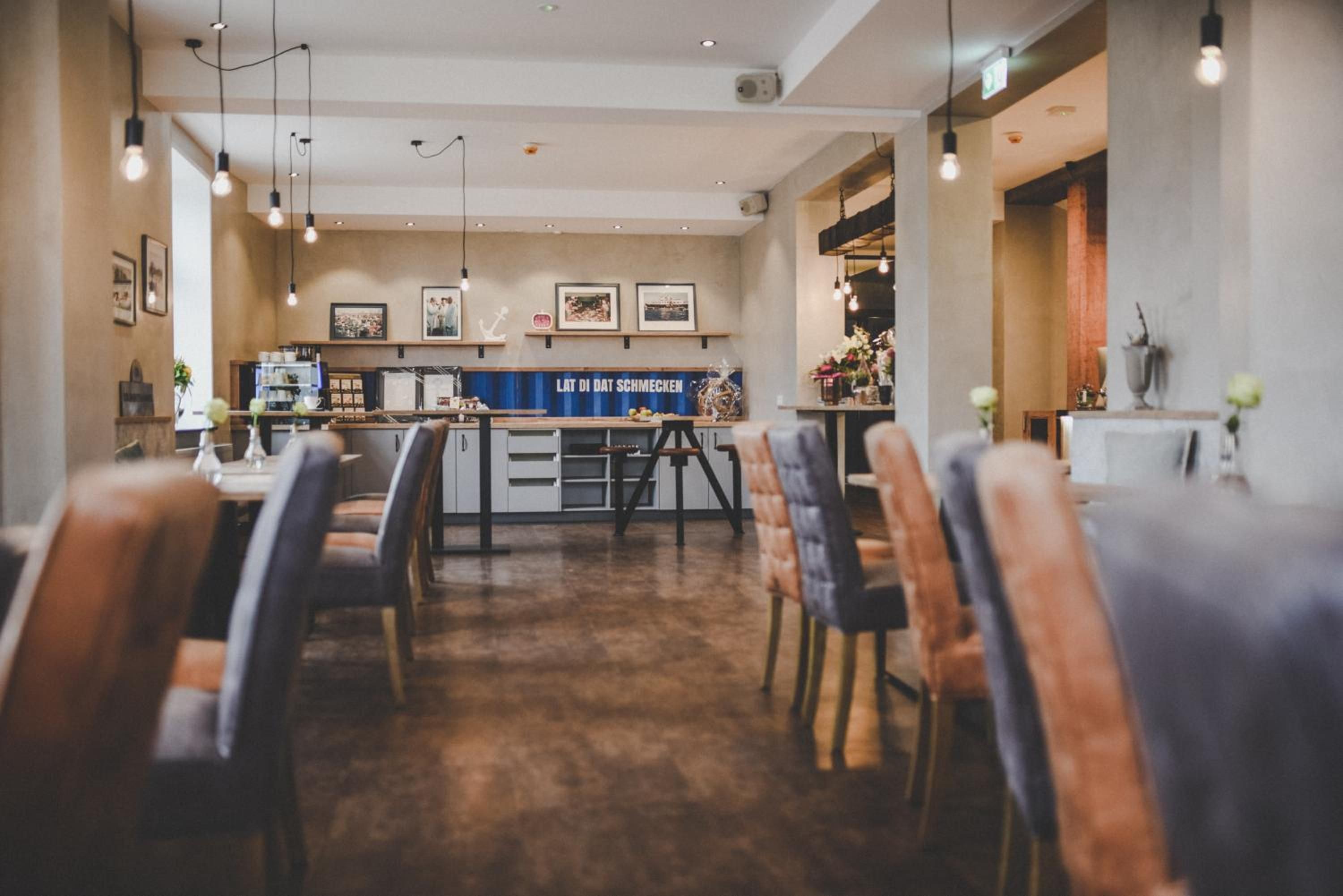 Ein Restaurantinneres mit Barbereich, Esstischen, Stühlen und hängenden Leuchten.