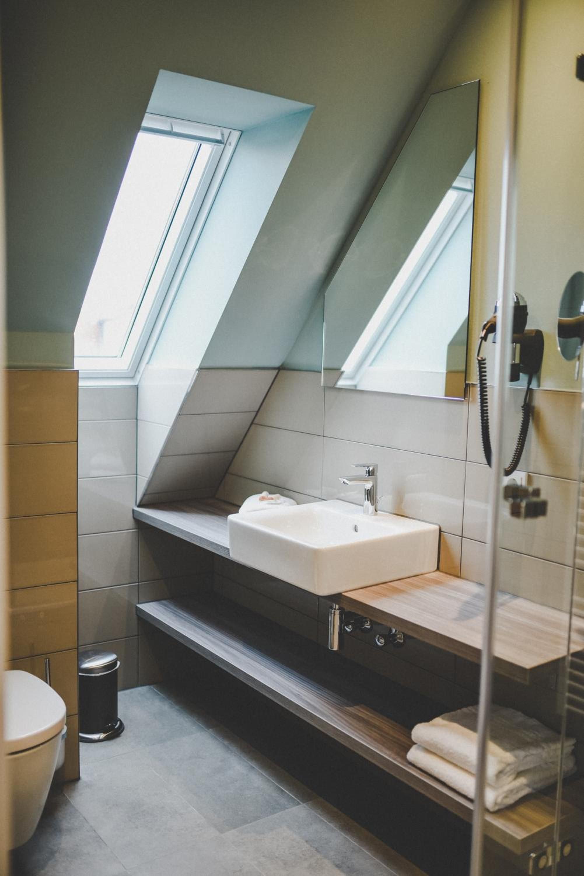Ein modernes Badezimmer mit Dachfenster, Waschbecken, Spiegel und Toilette.