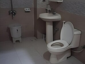 A small bathroom with a toilet, sink, and trash bin. - Hotel De Mall (Rawalpindi)