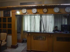 A reception area with a wooden counter, multiple clocks, and a sign indicating a cashier and reception. - Hotel De Mall (Rawalpindi)