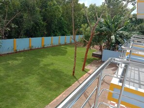Un espacio verde cuidado con césped, una pared azul y amarilla, árboles y una barandilla de metal.