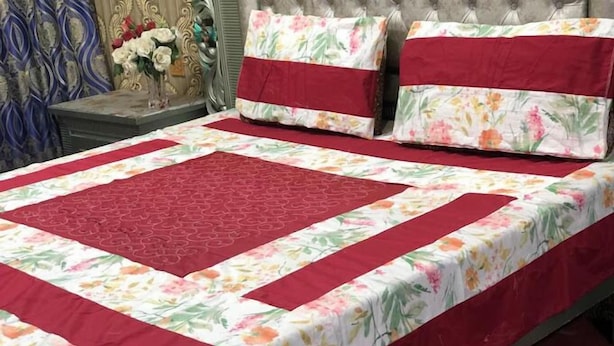 Een bed met een bloemenprint deken en rode accenten, omlijst door twee kussens met vergelijkbare dessins.