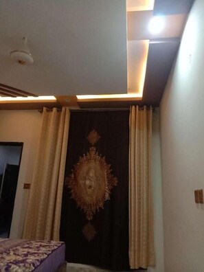 A room with a bed, a ceiling light fixture, and a tapestry. - Ntp Palace Hotel (Lahore)
