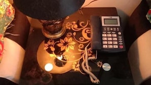 Een nachtkastje met een lamp, een telefoon en een decoratief bord.