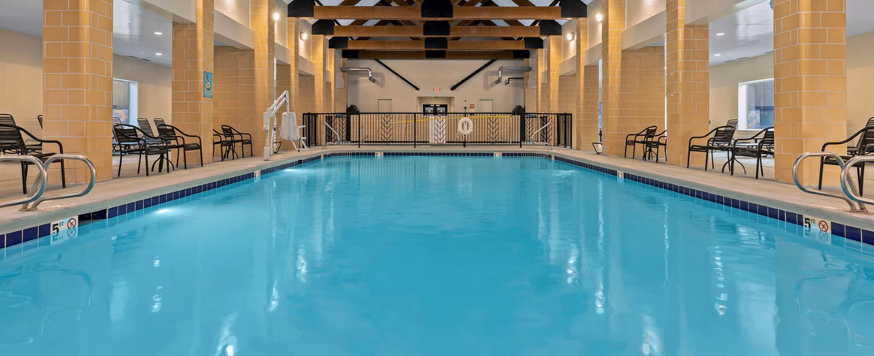 Una piscina interna con bordo piastrellato, circondata da sedie e da una postazione di salvataggio.