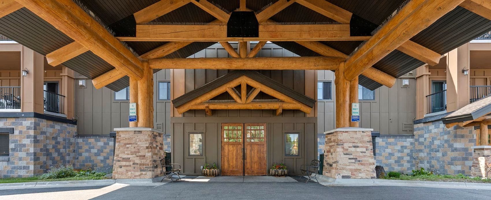A building entrance with a wooden overhang, stone pillars, and a double door.