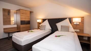 A hotel room with two single beds, a wooden wardrobe, a mirror, and bedside lamps.
