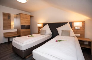 Habitación de hotel con dos camas individuales, un armario de madera, un espejo y lámparas de noche.