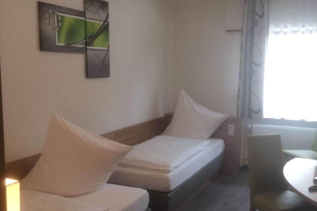 A room with two single beds, a chair, a table, and a window with curtains.