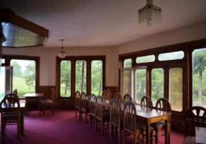A dining area with a long table and chairs, large windows, and a chandelier.