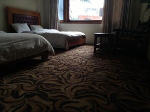A hotel room with two beds, a small table, and a window with curtains.
