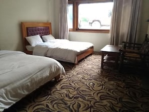A hotel room with two beds, a patterned carpet, a window with curtains, and a small table.