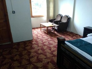 A room with a bed, two armchairs, a small table, and a window with curtains.