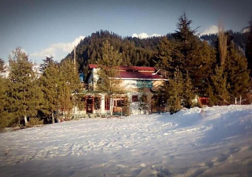 A building with a red roof, surrounded by snow-covered ground and trees, with a mountainous backdrop.