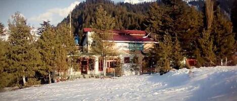 A building with a red roof, surrounded by snow-covered ground and trees, with a mountainous backdrop.