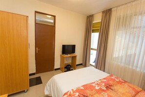 Habitación de hotel con cama, televisor sobre un mueble, armario y ventana con cortinas.