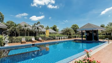 A swimming pool with lounge chairs and a gazebo, surrounded by greenery and buildings.