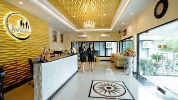 A hotel reception area with a modern design, a reception desk, a chandelier, and a large window offering a view of the outdoors.