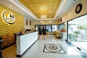 A hotel reception area with a modern design, a reception desk, a chandelier, and a large window offering a view of the outdoors.