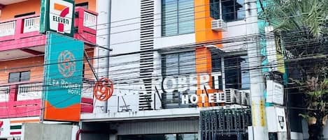 A hotel with a 7-Eleven convenience store on the ground floor, a visible entrance, and parked cars in front.